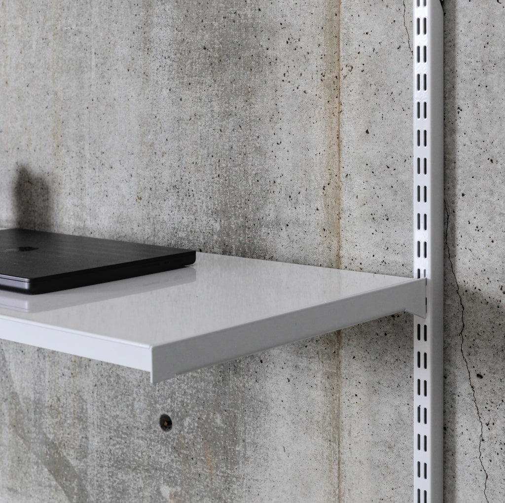 Close-up of white steel shelf surface with folded edge supporting laptop in wall-mounted shelving system