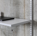 Close-up of white steel shelf surface with folded edge supporting laptop in wall-mounted shelving system