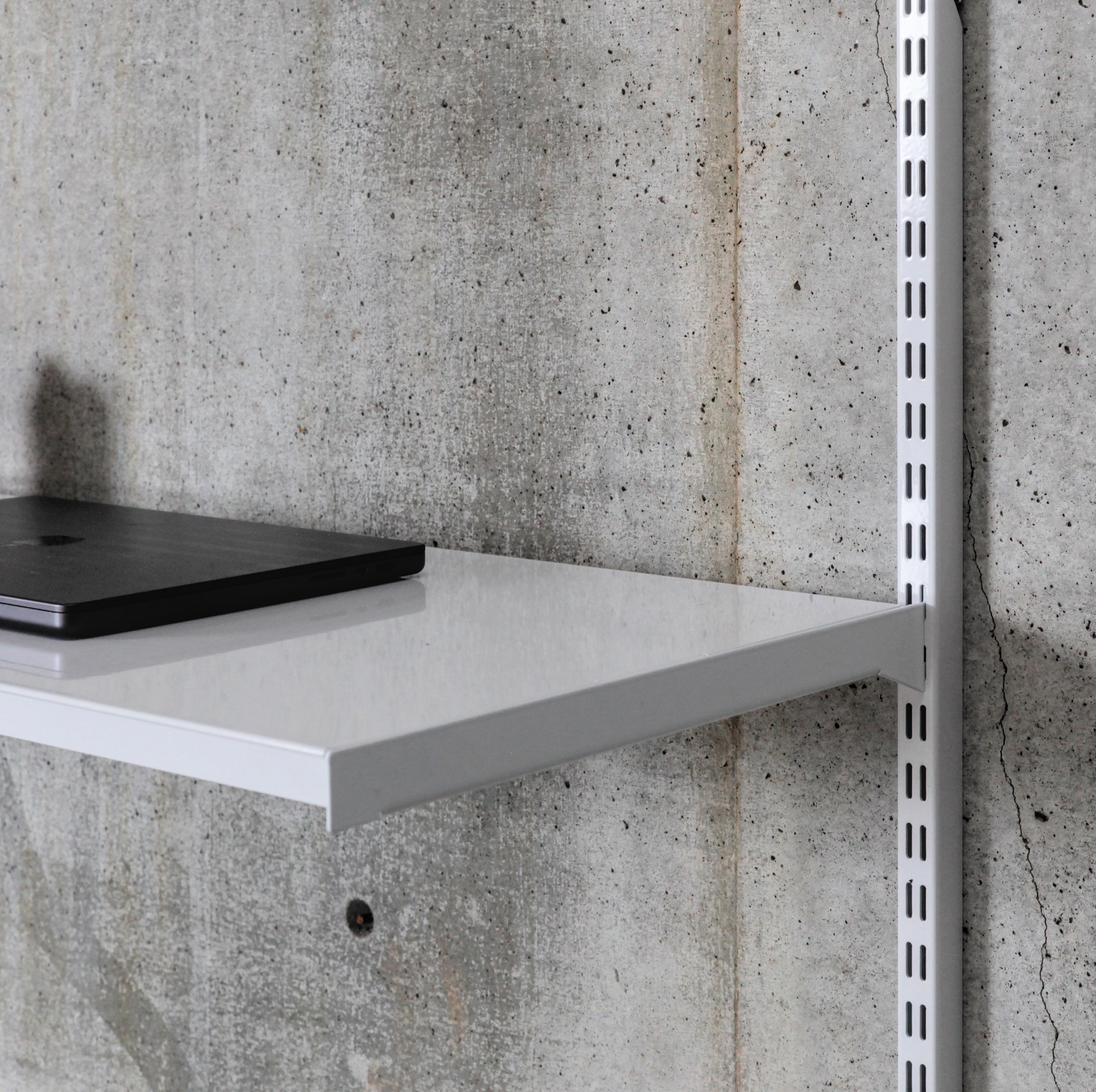 Close-up of white steel shelf surface with folded edge supporting laptop in wall-mounted shelving system