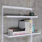 Modular wall-mounted shelving with steel shelves holding books and decor against concrete wall