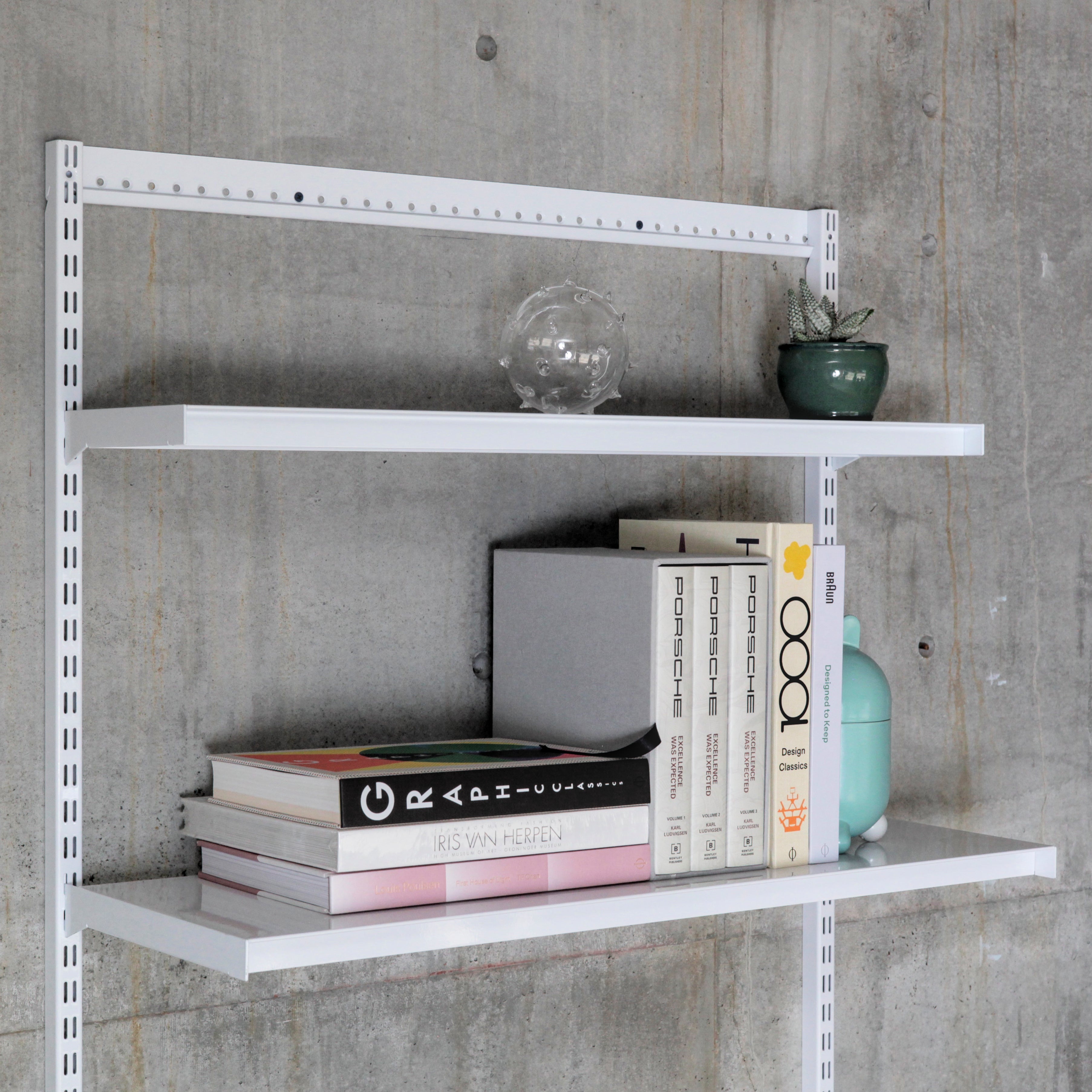 Modular wall-mounted shelving with steel shelves holding books and decor against concrete wall