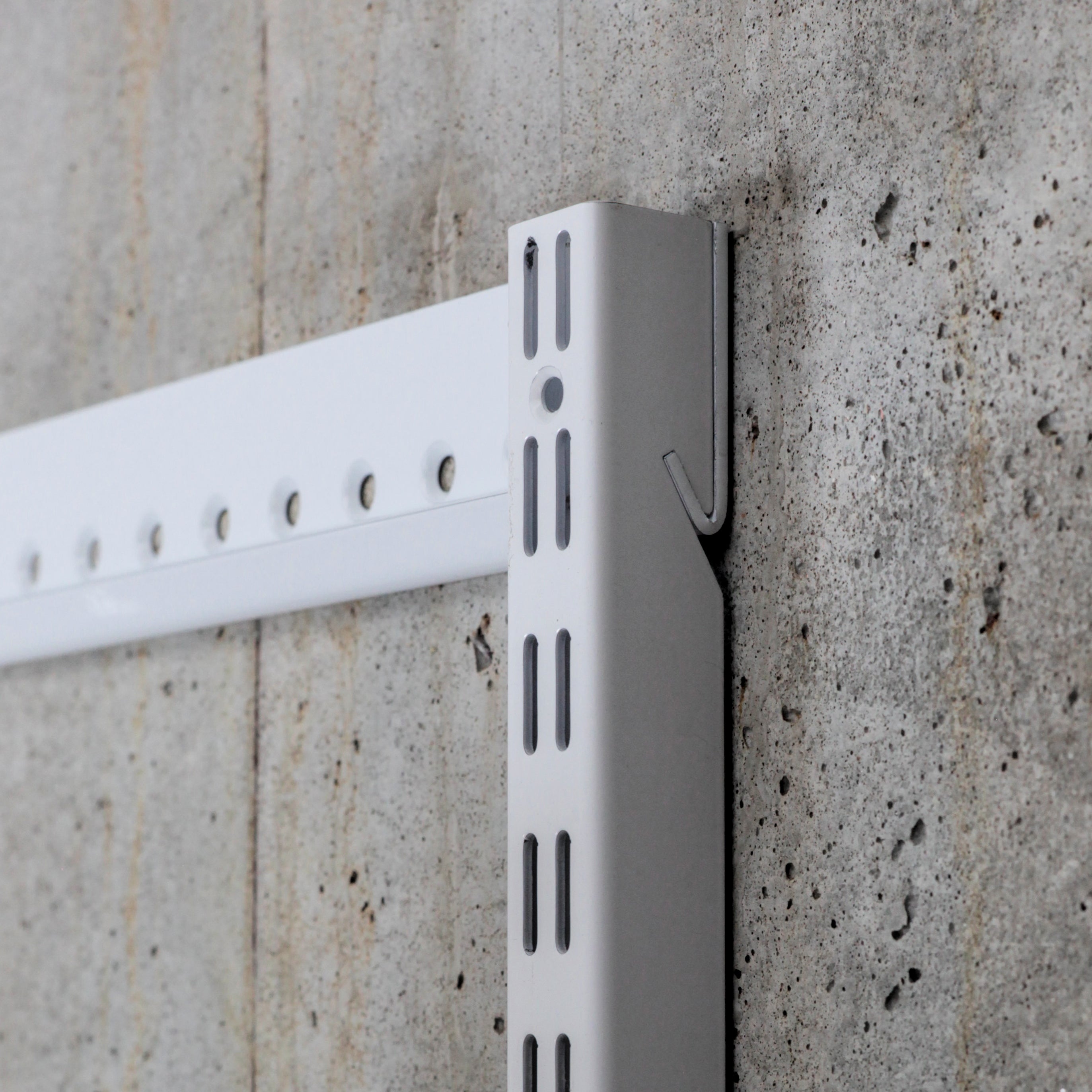 Close-up of steel shelving standard and wall-mounted hangtrack showing slot detail and mounting system