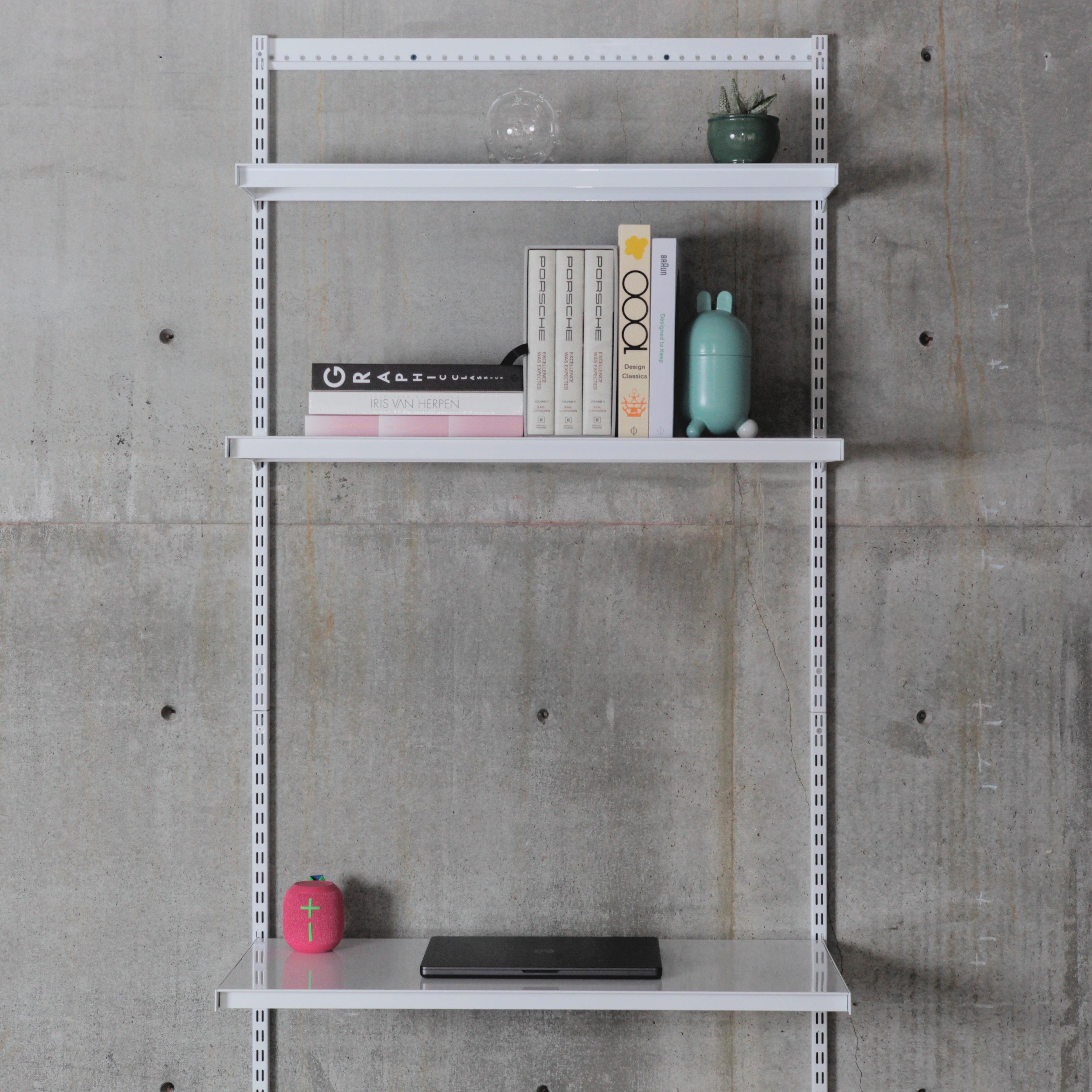 Modular wall-mounted shelving system with three steel shelves, books above and laptop on lower shelf